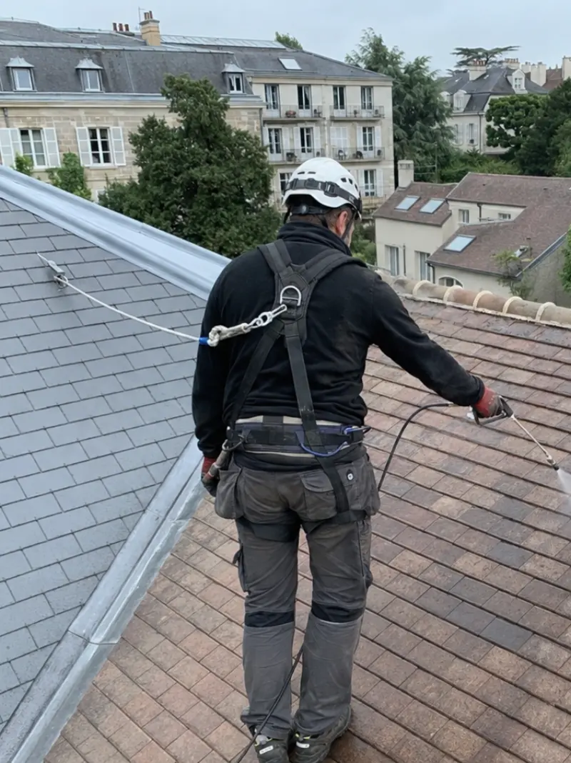 Couvreur DV Rénotoit harnaché et assuré par ligne de vie, en cours de traitement d'une toiture en tuiles.